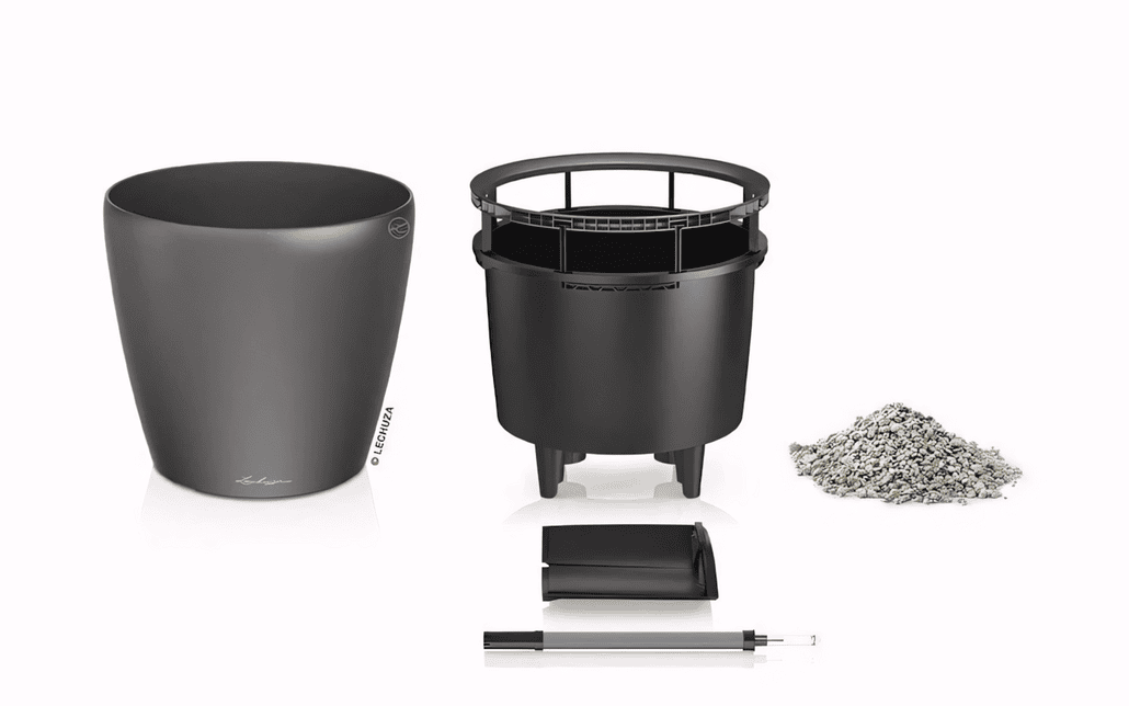 Czarna doniczka samonawadniająca pokazana w stanie rozmontowanym z wewnętrznym zbiornikiem na wodę, stosem podłoża, wskaźnikiem poziomu wody i separatorem, wszystko na białym tle.