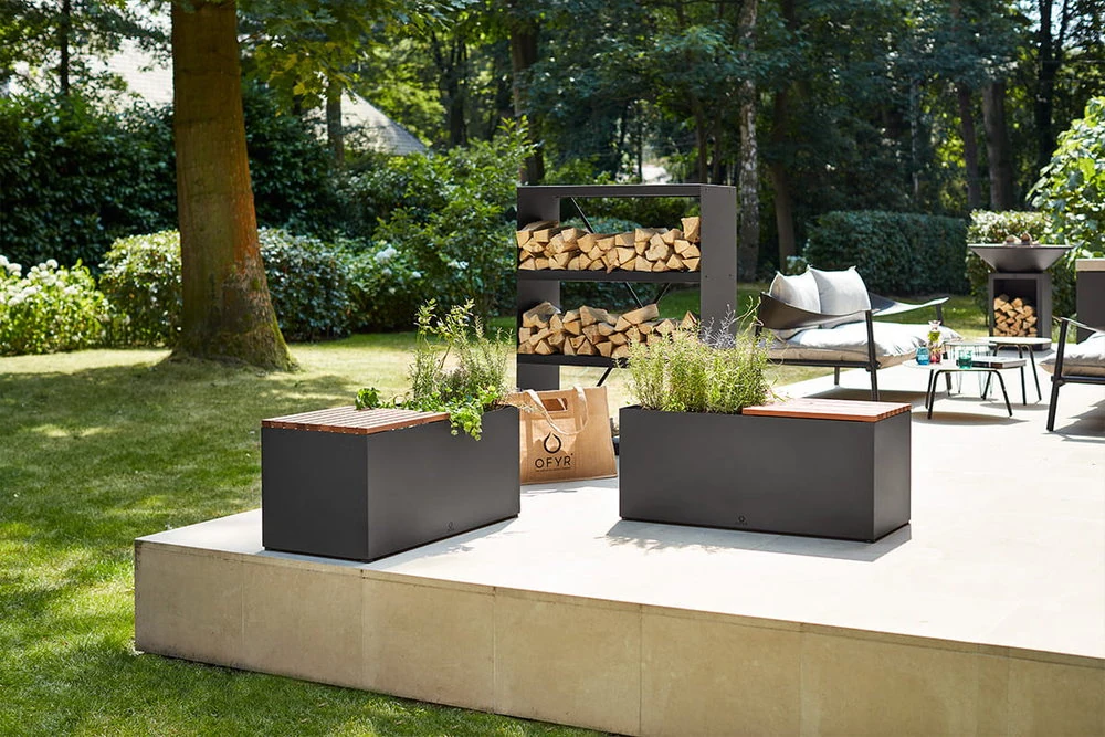 Dwie czarne ławki Ławka HERB BENCH z pojemnikiem na zioła, drewnianymi listwami i roślinami na patio.