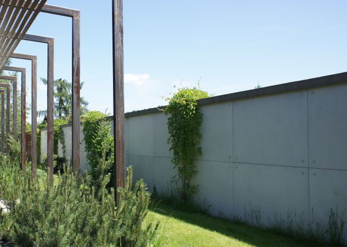 Szare płyty elewacyjne z betonu architektonicznego z widocznymi punktami mocowania przy ścieżce i pergoli.
