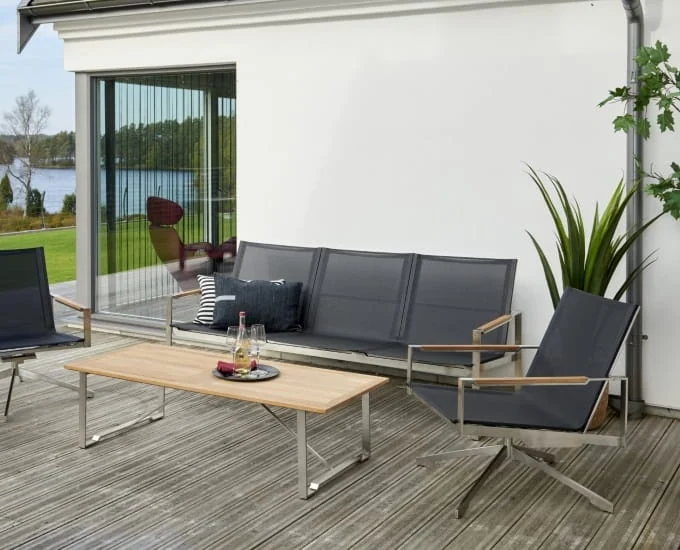Stalowa sofa trzyosobowa „Gotland”, dwa fotele obrotowe i prostokątny stolik kawowy na tarasie.