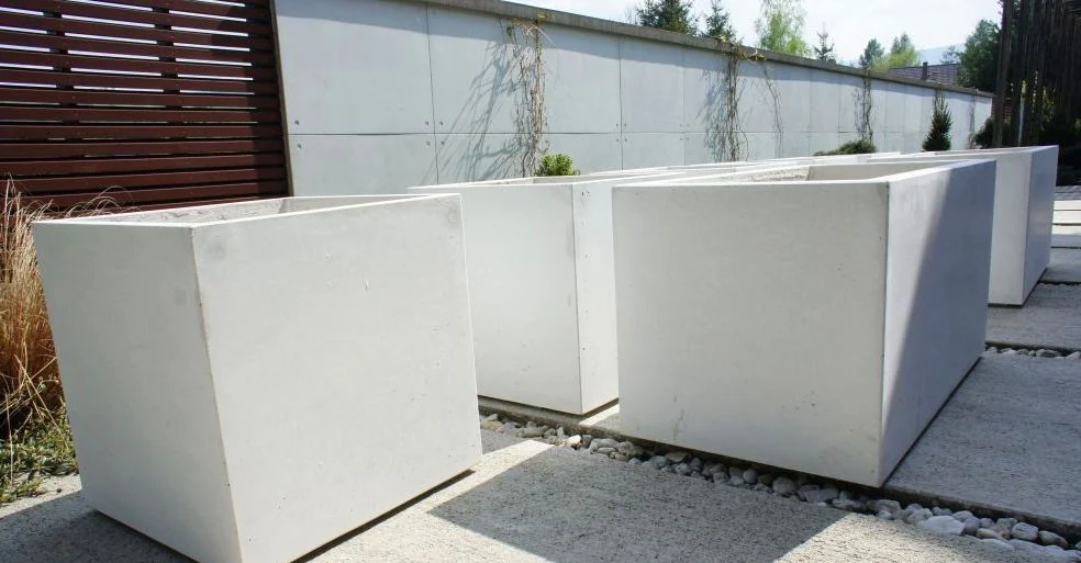 Trzy prostokątne donice – nowoczesna donica betonowa o wymiarach 80 x 80 x 100 cm (wys.) ustawione w rzędzie na tarasie.