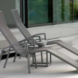 Dwa szare leżaki, aluminiowy leżak „Balance” z podłokietnikami oraz stolik z dwoma kubkami na tarasie wyłożonym płytkami.