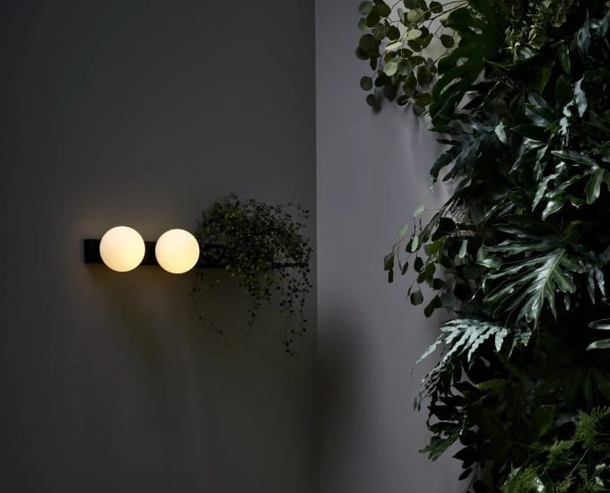 Kinkiet „Botanica” z dwiema kulistymi żarówkami i półką z wiszącą rośliną.