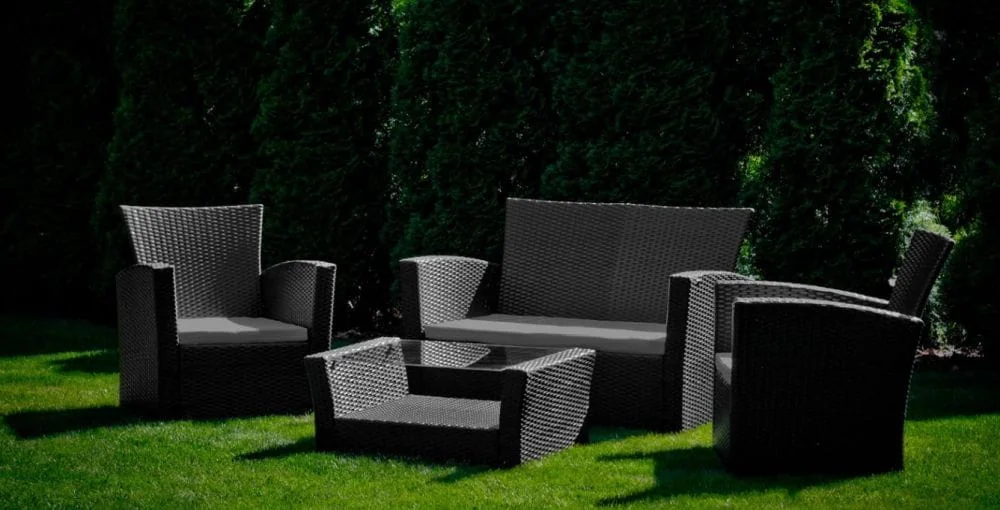 Zestaw mebli ogrodowych UNICO: sofa, dwa fotele i niski stolik kawowy z szarymi poduszkami na zielonym trawniku.