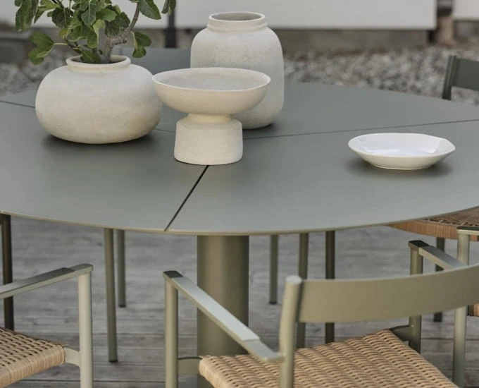 Okrągły stół „Peace 150” z ceramicznymi wazonami i białą miseczką, otoczony fotelami z plecionymi siedziskami.