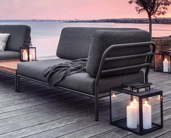 Ciemnoszara sofa narożna „Level” (prawa) z oparciem i boczną listwą na drewnianym tarasie z lampionami o zmroku.