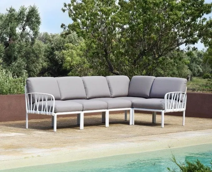 Modułowa sofa narożna Komodo marki Nardi, z białą ramą i szarymi poduszkami na tarasie przy basenie.