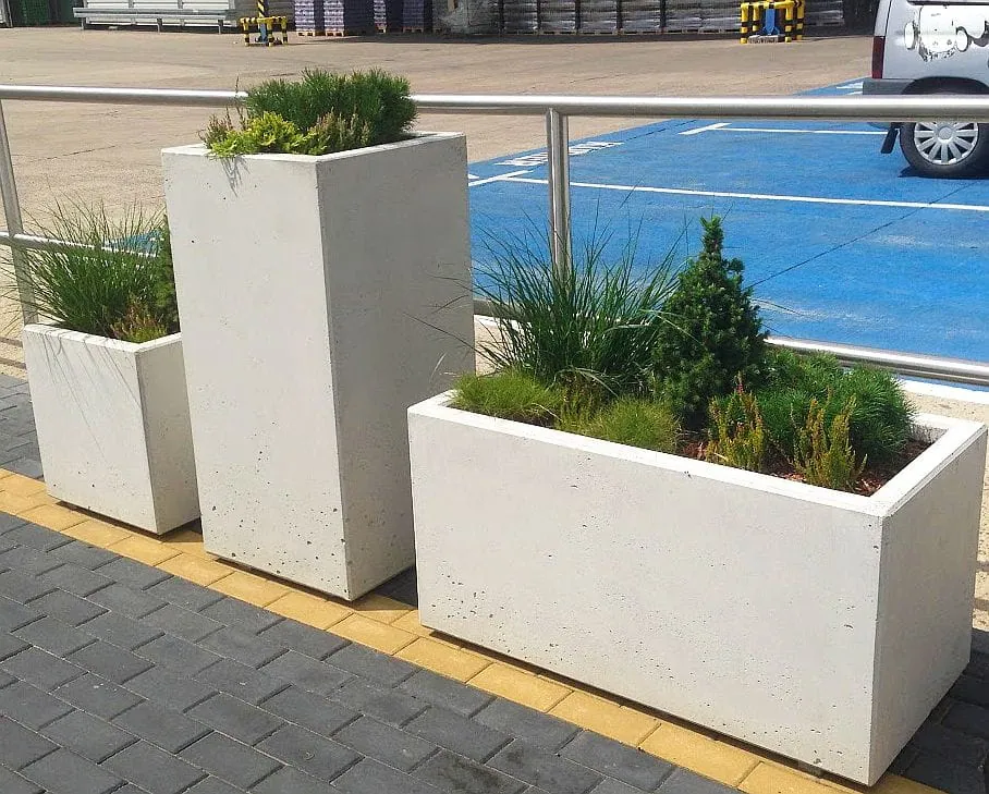 Trzy prostokątne, jasnoszare donice „Betonowa” o wymiarach 100 x 50 x 40 cm i różnej wysokości, z krzewami iglastymi i trawami.