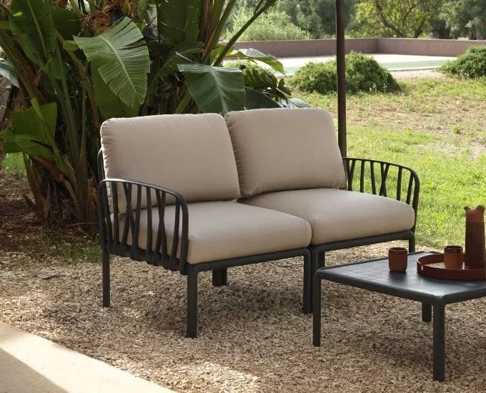 Dwuosobowa sofa ogrodowa Nardi Komodo z beżowymi poduszkami i ciemną ramą przy dopasowanym stoliku na tarasie pokrytym żwirem.