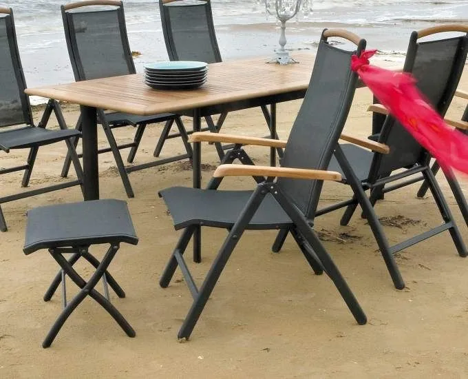 Zestaw składanych krzeseł, stolik i mały stołek na piaszczystej plaży, w tym rozkładany fotel aluminiowy „Rennes”.