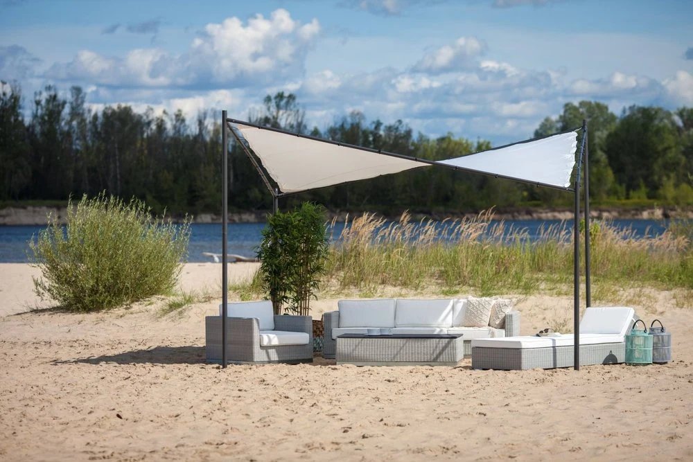 Zestaw wypoczynkowy pod trójkątnym żaglem ogrodowym „Butterfly” na piaszczystej plaży nad rzeką.